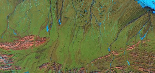 Landsat 7 false-color image of the North Slope. Along the coast, fast ice still clings to the shore in a solid, frozen sheet. At the top of the scene is the drifting sea ice. A dark blue strip of open water, known as a flaw lead, separates the fast ice from the drifting sea ice. The Brooks Range is visible at the bottom. (June 2001)